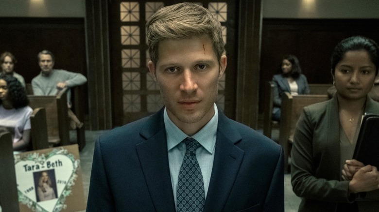 Riley wearing a suit and frowning in a courtroom in 