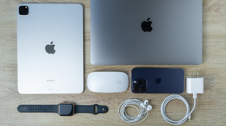 a macbook, iPad Pro, Apple Watch, iPhone, magic mouse, earphones and charging adpater placed on a wooden table
