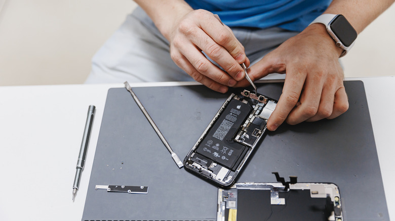 person wearing an Apple Watch repairing an iPhone with specialized tools placed on the table