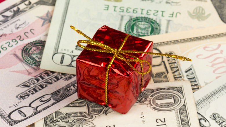 A small red gift with gold string sitting atop a pile of money of random denominations