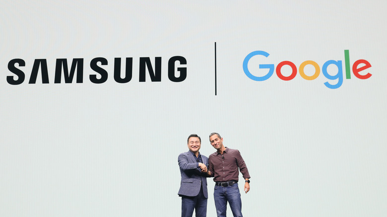 Samsung and Google logos above two executives shaking hands on a stage.