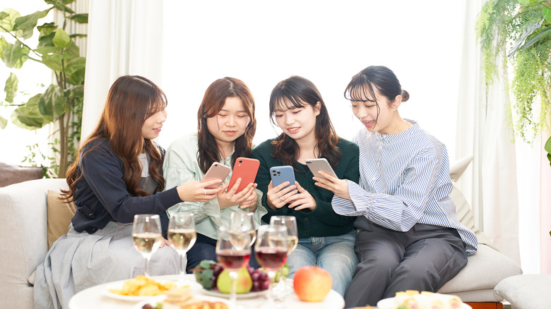 four women talking and looking at their smartphones at a party