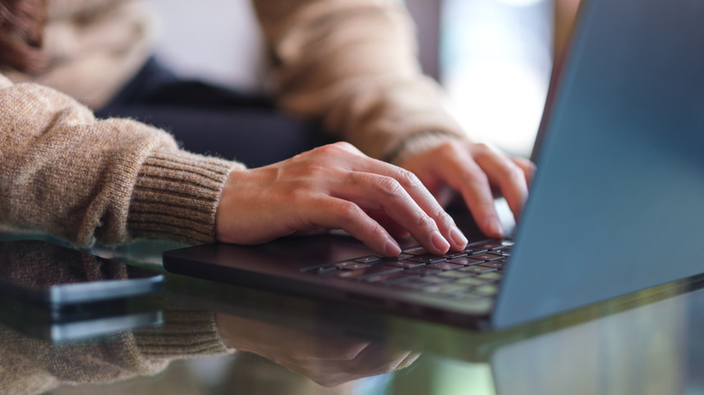 person working on a laptop placed on a glass table with a smartphone kept on the side