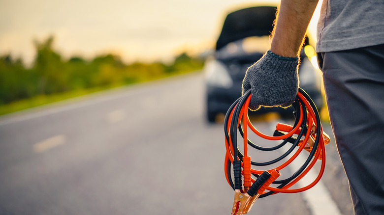 A person holding jumper cables in front of a car.