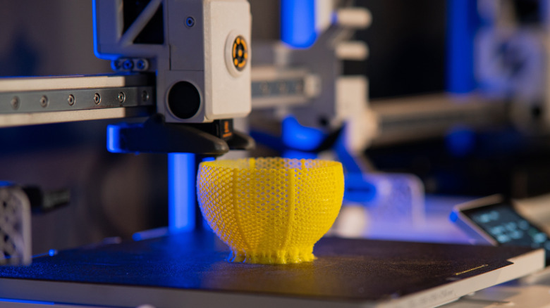 3D printer creating a yellow object on its print bed.