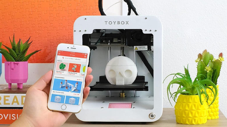 Toybox 3D printer creating a skull while a person holds the companion app.
