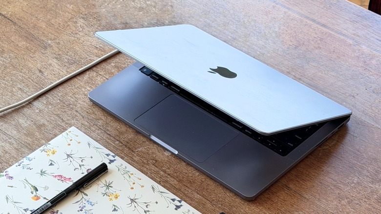 A MacBook Pro on a wood table with a little book and pen below it
