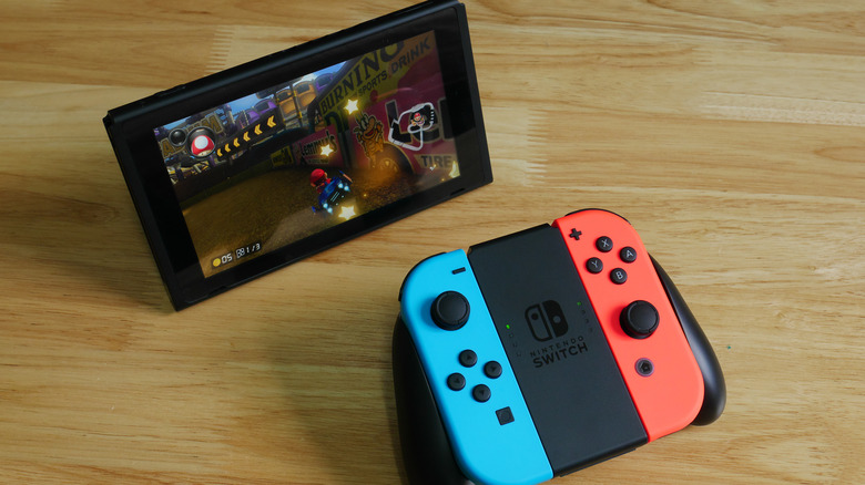 A Nintendo Switch console on a table in front of Joy-Cons in a grip.