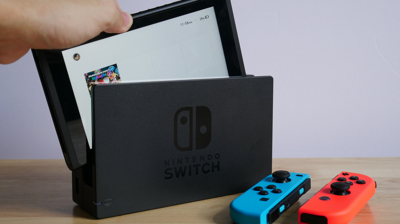 A person pulling a Nintendo Switch out of its dock in front of two Joy-Cons.