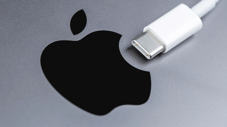 The tip of an Apple USB-C charging cable laying next to an Apple logo on a device