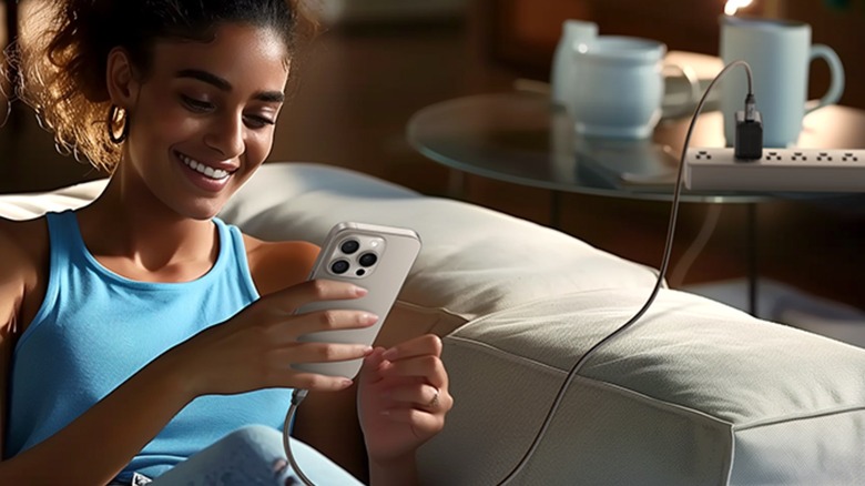 A person using a Silkland USB-C Monitor Display Cable to charge their iPhone while sitting on a gray couch