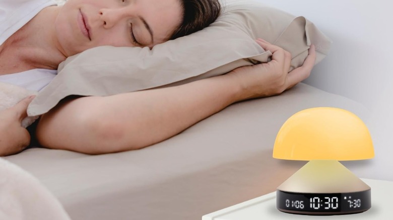 Lexon Mina Sunrise Alarm Clock on bedside table with woman sleeping on bed