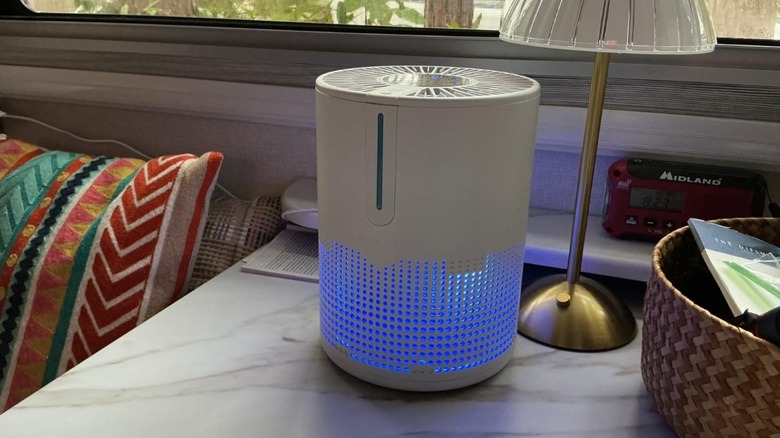 White Mooka air purifier with blue glow on a bedside table.