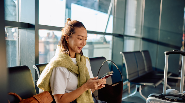 A woman using a smartphone in an airport terminal.