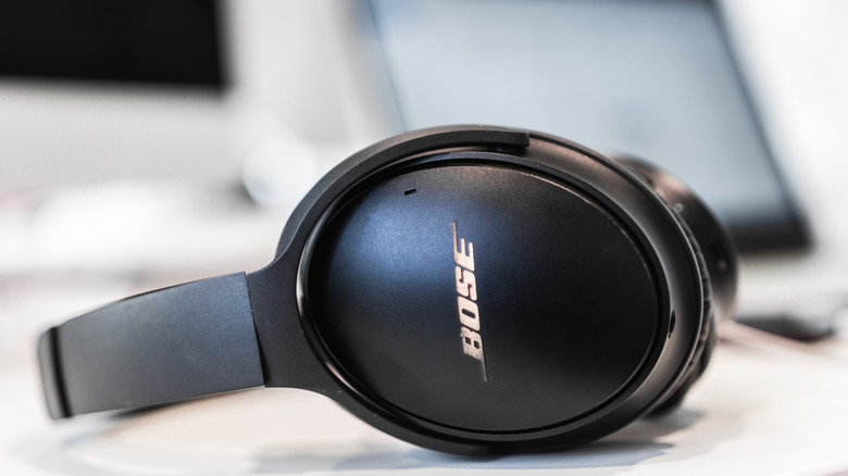 Bose headphones resting on a desk with a blurred monitor visible in the background.