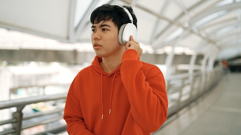 Man wearing headphones in public place, pressing finger to side.