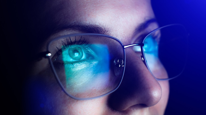 Blue light from a monitor reflecting into a person's glasses.