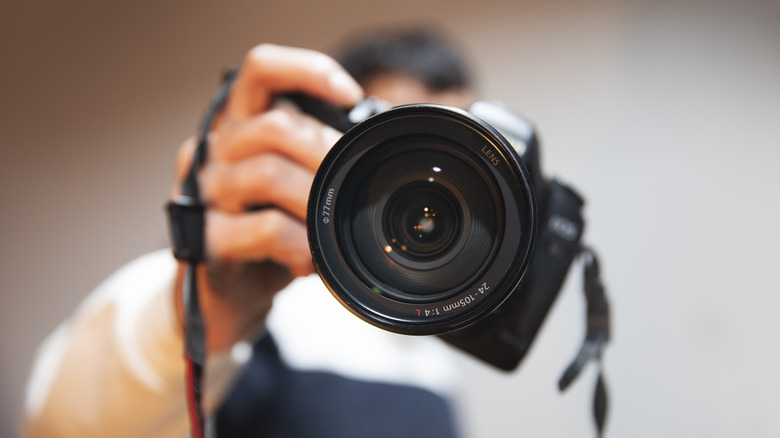 A black digital camera is being pointed directly at the camera, the image focuses on the lens of the camera being photographed