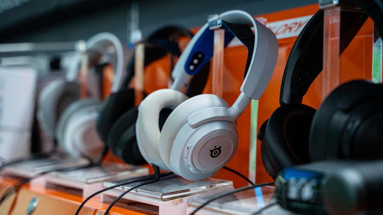 A closeup of a pair of white SteelSeries headphones sitting next to two blacks pairs and a what appears to be another white pair, the headphones are displayed in a store