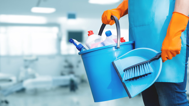 Person holding a bucket filled with cleaning supplies