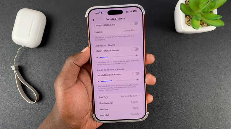 Hand holding iPhone showing separate volume sliders for alarms and system sounds