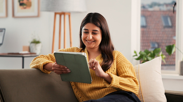A woman sitting on a couch smiling while using an iPad