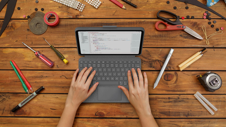 Close up of hands typing on an iPad in a gray keyboard case on a wooden table surrounded by tools