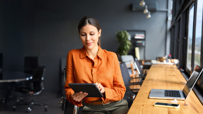 A woman sitting at her desk checking an iPad with other Apple devices next to her.