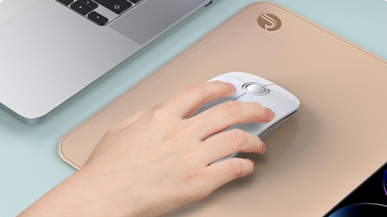Close up of a hand using a white mouse on a beige mouse pad with a MacBook