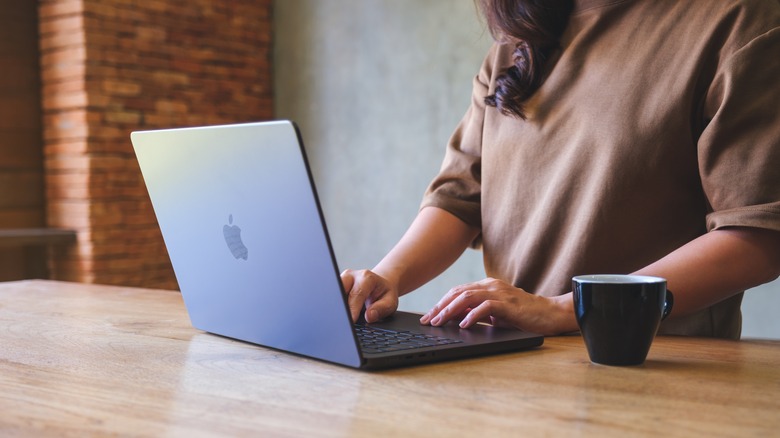 a woman typing on a macbook with a cup placed next to her