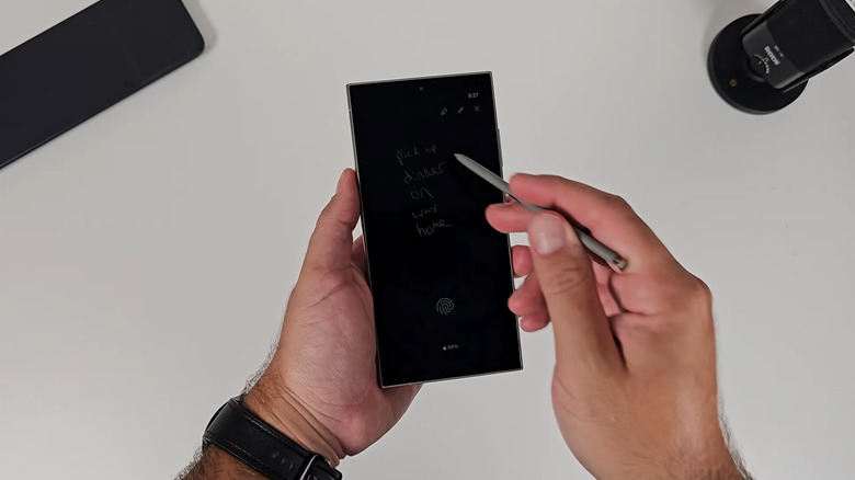 Hand holding phone with pinned handwritten note on screen
