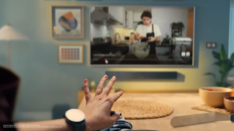 Hand with Samsung Galaxy Watch doing pinching motion in front of Samsung TV