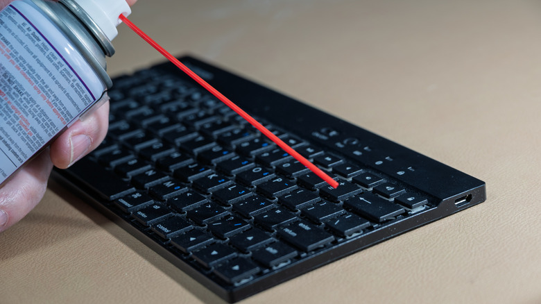 A person cleaning a keyboard with a can of compressed air.