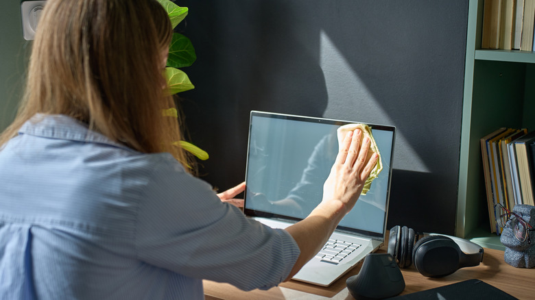 A woman wiping down a laptop screen.