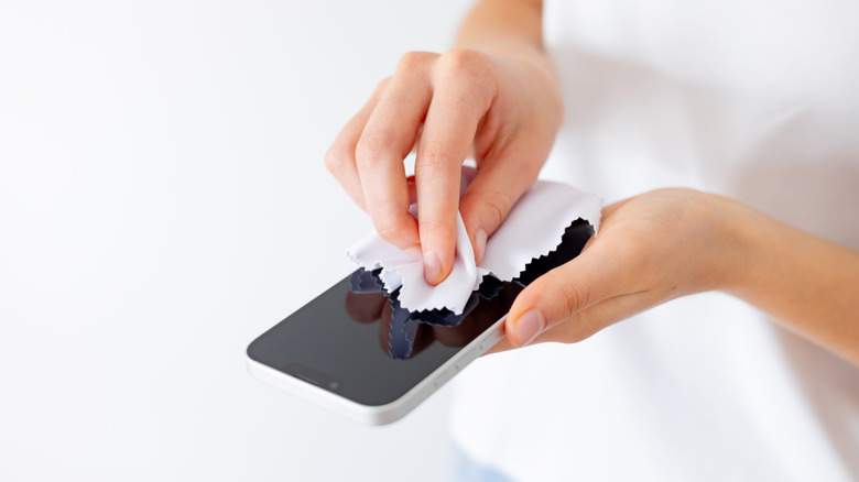 A person cleaning a phone screen with a microfiber cloth.