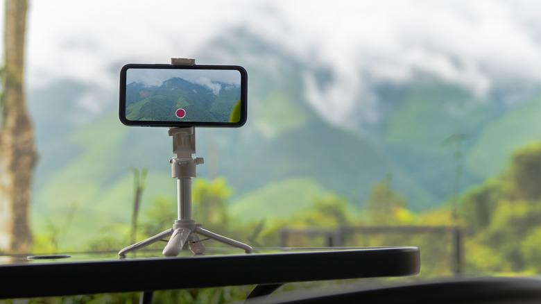 A smartphone on a plastic tripod with its camera focused on some mountains.