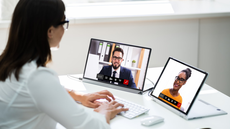 Woman at desk in conference call with two laptop screens