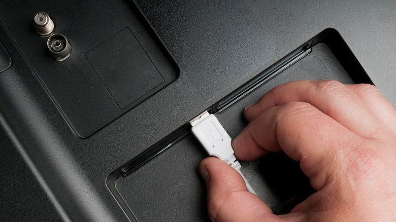 a hand plugging a USB cable into the back of a TV