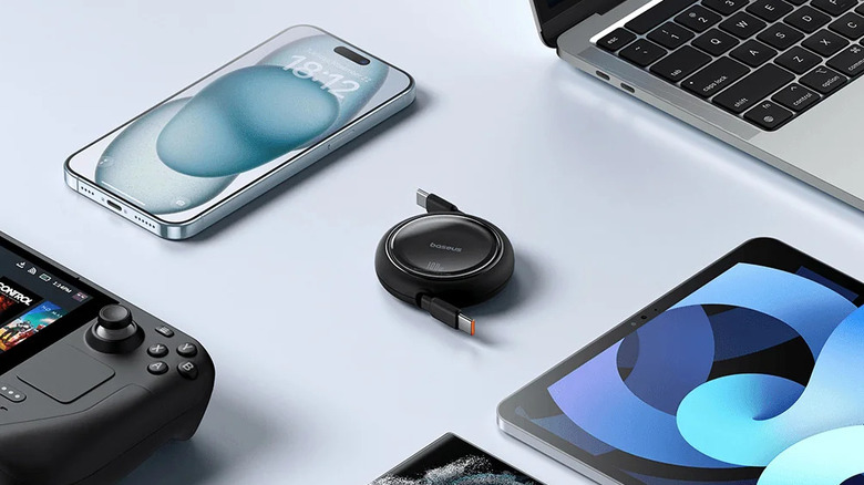 A round retractable Baseus USB-C cable surrounded by various devices, including an iPhone, MacBook, and Steam Deck