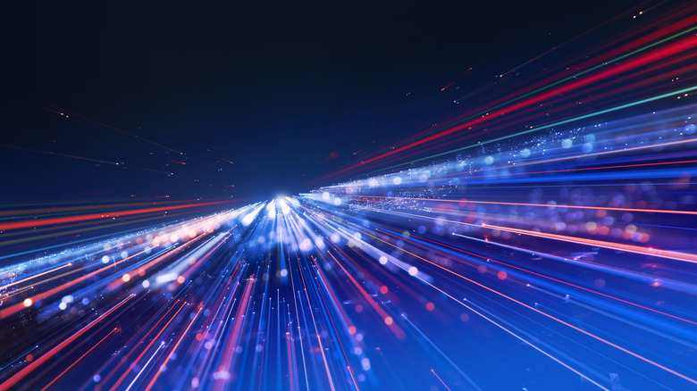 Glowing lines bursting out of a distant light on a dark background to represent fast motion or technology