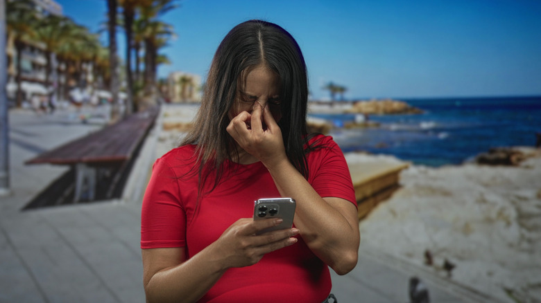 Woman holding nose while using a smartphone on a beach