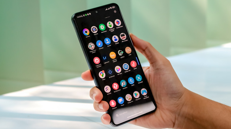 A person holding an Android phone with the app drawer open, revealing a list of app icons.