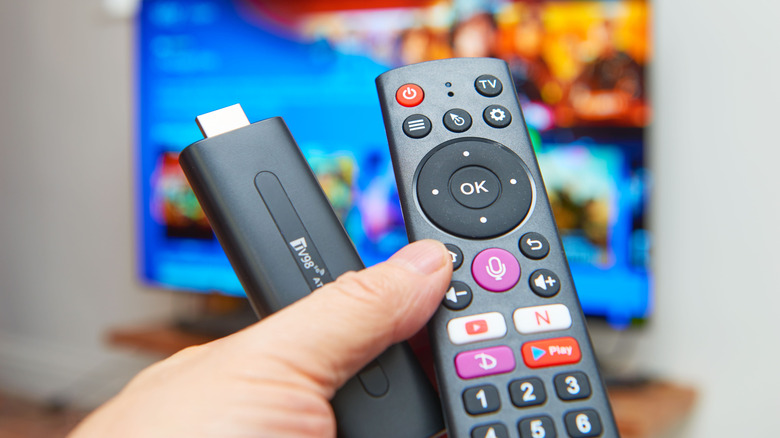 A person holding a remote and streaming stick in front of a TV.
