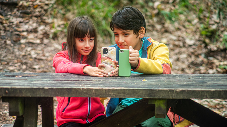 Two kids at a picnic table looking at iPhones