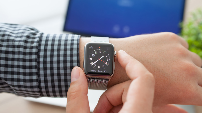 Using an Apple Watch with a MacBook in the background.