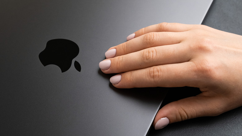 A person about to open the lid of a MacBook.