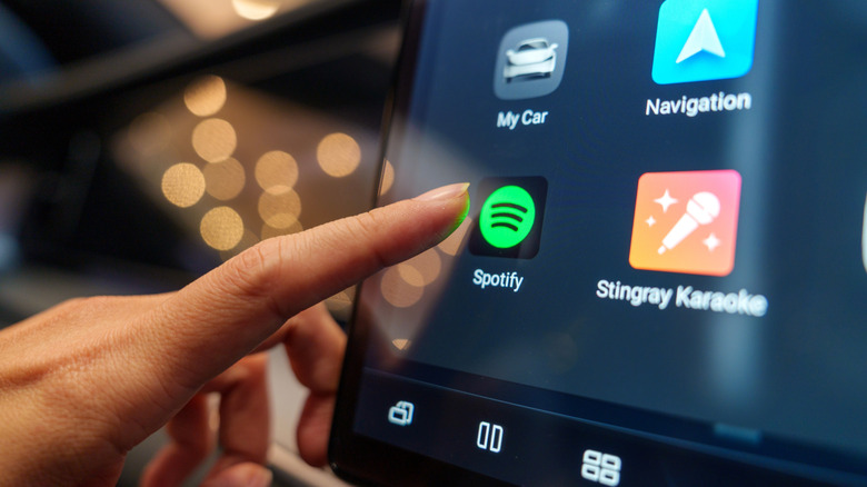 Finger selecting Spotify on a car infotainment screen.