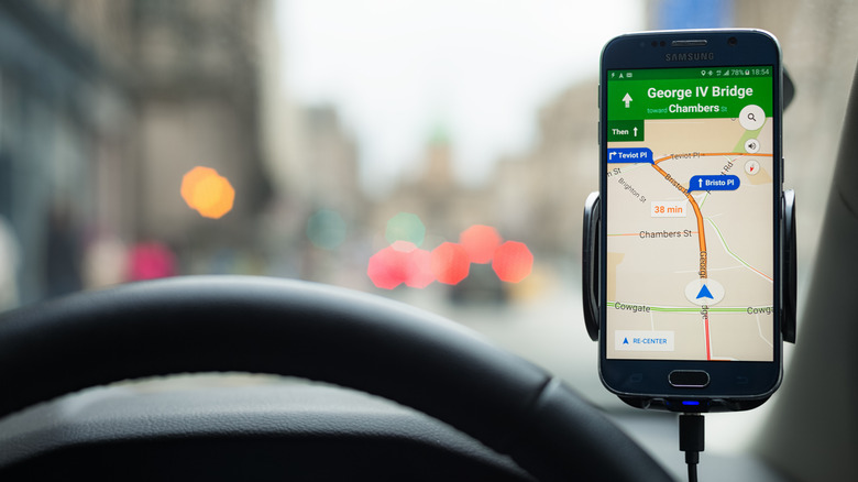 Smartphone showing Google Maps navigation mounted inside a car.