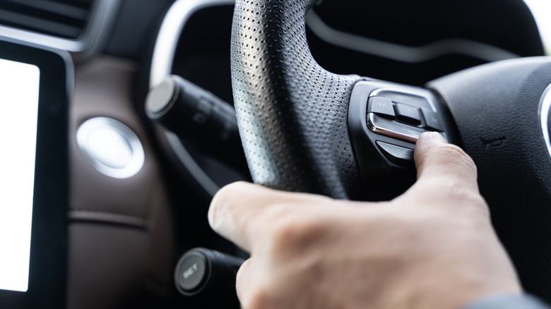 Driver pressing buttons on a car steering wheel.