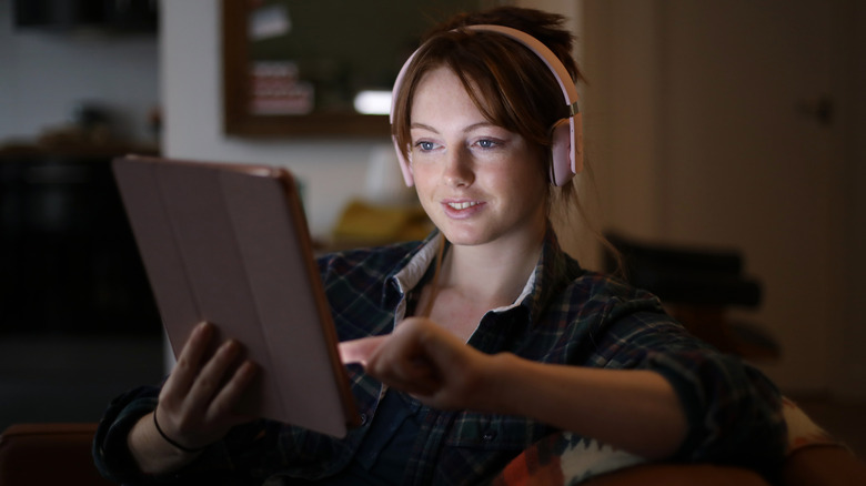 A person listening to audio via an iPad using a pair of headphones